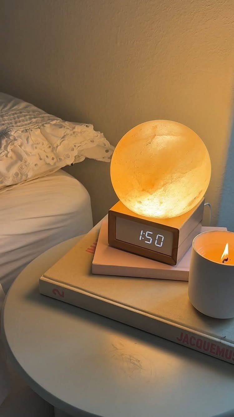 Glowing moon lamp and lit candle on a white bedside table next to a bed