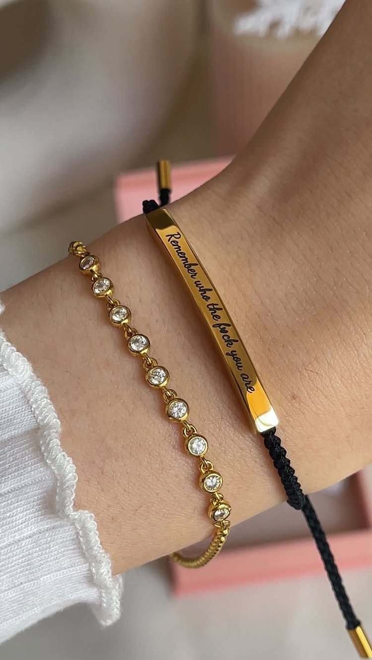 Two bracelets on a wrist, including a gold bar with an engraved message.