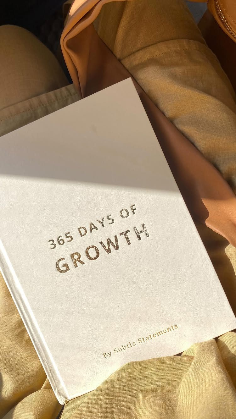 White hardcover growth journal resting on tan fabric next to a leather bag.