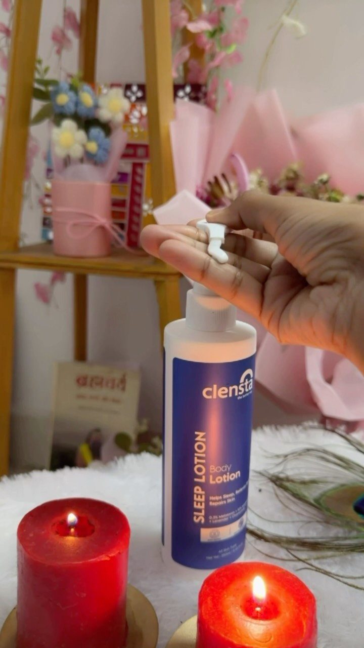 Hand dispensing sleep body lotion from a pump bottle next to red candles.