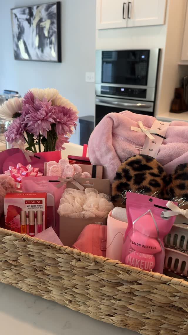 Woven basket filled with pink robe, leopard slippers, and beauty products with flowers.