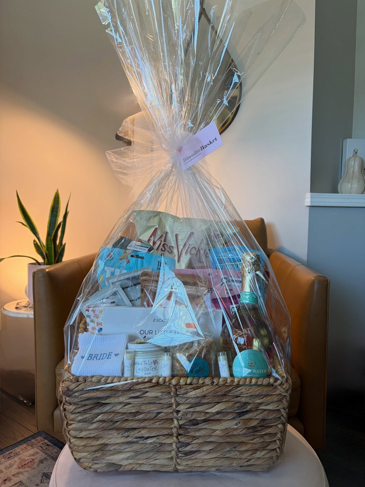 Woven gift basket with champagne and beauty products wrapped in clear cellophane.