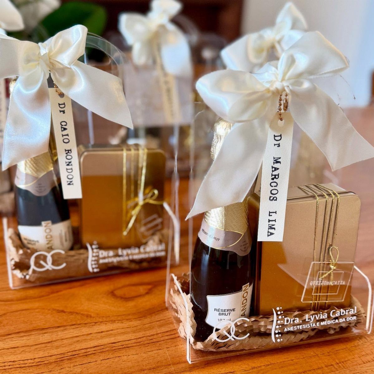 Personalized wine gift baskets with gold boxes and white satin bows on wood.