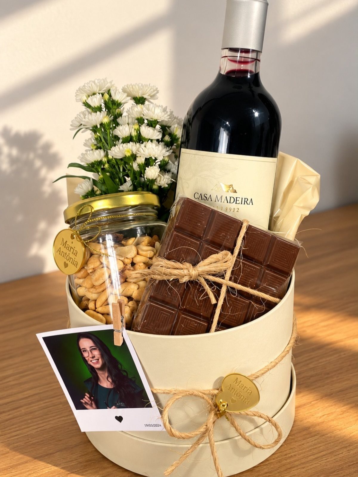 Wine and chocolate gift basket with nuts, white flowers, and a personal photo.